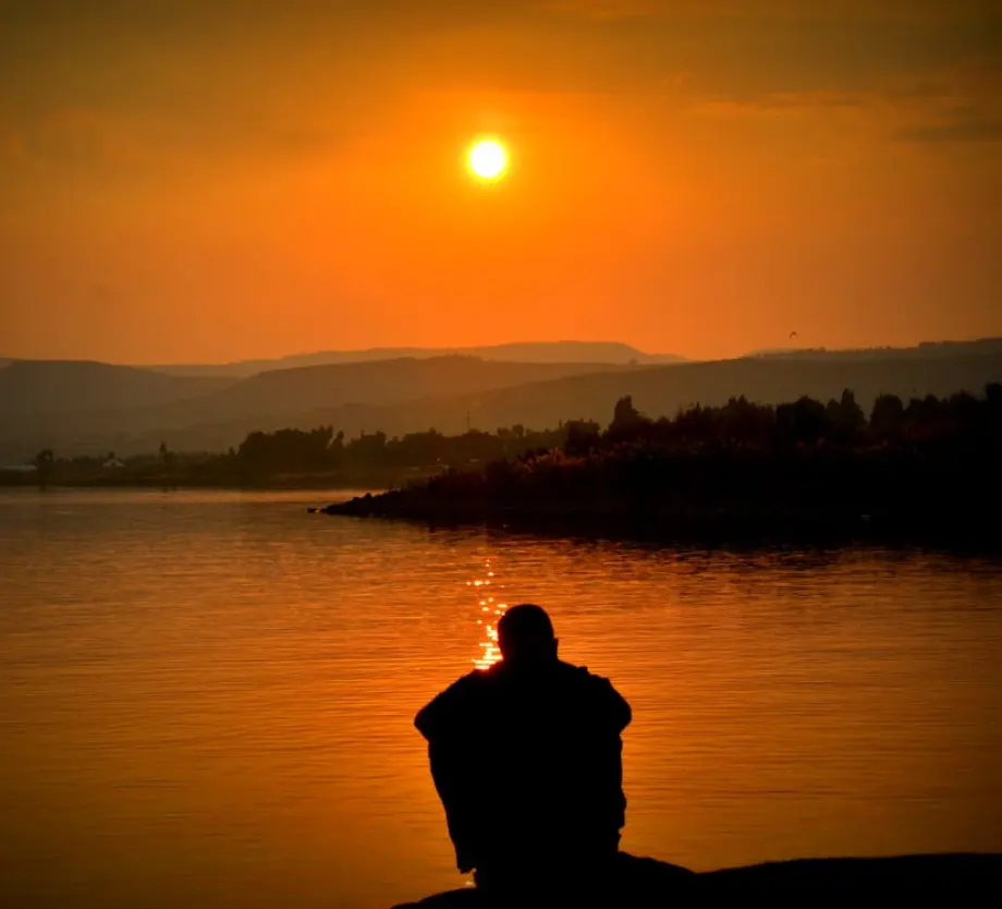 Man sitting by the waters edge looking at the sunset